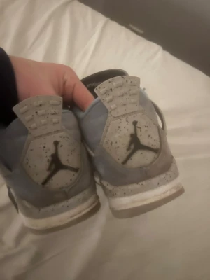 Air Jordan 4 Retro University Blue - Säljer ett par Air Jordan 4 Retro University Blue sneakers med ljusblå mocka, grå detaljer och svart Jumpman-logga på hälen. Skorna har vita och grå sulor med svarta stänk och klassisk Air Jordan-tunga. Perfekta för dig som gillar streetwear och snygga detaljer.