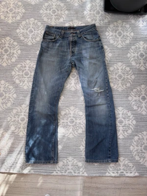 Nudie jeans bootcut  - Storleken är 31/34 och modellens namn är bortslitet. 99%säker på att det är bootcut ola eftersom jag hade ett par innan och de exakt samma. Säljer ett par klassiska blå jeans från Nudie Jeans med bootcut passform och slitningar på höger lår. Jeansen har fem fickor, tydliga sömmar och en snygg tvättad look. Perfekta för en avslappnad stil. 