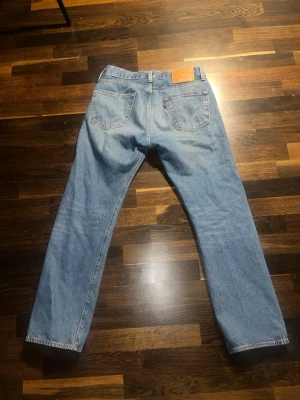 Levi's 501 - Klassiska ljusblå jeans från Levi's med raka ben och femficksmodell. Jeansen har en avslappnad passform och tydliga sömmar, samt Levi's ikoniska läderpatch bak i midjan. Perfekta för en casual och tidlös stil.