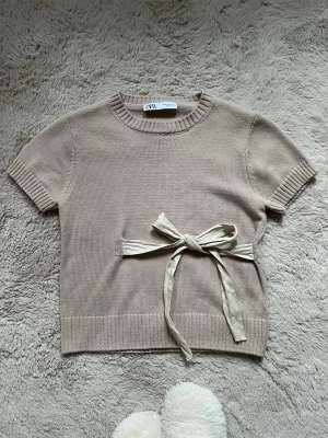 Beige stickad topp från Zara - Kortärmad stickad topp från Zara i beige med rund halsringning och ribbade kanter. Inte nopprig och i super fint skick 