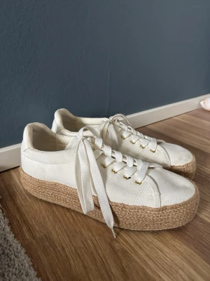 Vita platåsneakers med jutesula - Säljer dessa super snygga vita sneakers från H&M med platåsula i flätad jute och ovandel i canvas. Skorna har vita skosnören och guldfärgade öljetter som ger en fräsch och trendig look. Storlek 41, men passar mer som 40/41!! Skorna var använt bara en gång, inga defekter. Perfekta för dig som vill ha en stilren men ändå unik sneaker, men även nu inför vår!💐💞