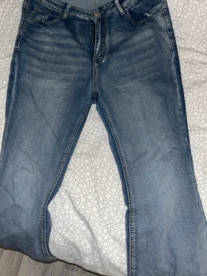 Blå bootcut jeans med slitningar - Säljer ett par klassiska blå jeans med raka ben och snygga slitningar framtill. Jeansen har fem fickor, bälteshällor och dragkedjegylf. Perfekta för en avslappnad och trendig look. Materialet är denim i bomull.