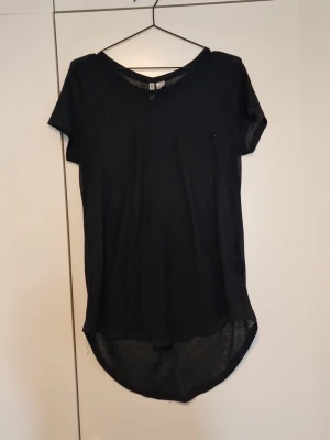 Svart t-shirt med längre bakdel - Svart t-shirt från H&M med rund halsringning och korta ärmar. Modellen är längre baktill för en modern look. Tillverkad i ett tunt och mjukt material som känns skönt mot huden. Perfekt för en avslappnad och stilren outfit.