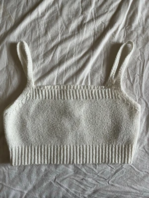 Vit stickad linnetopp - Säljer en vit stickad linnetopp med bred ribbad kant nedtill och smala axelband. Perfekt att styla med höga jeans eller kjol för en chill och trendig look.