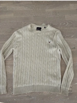 Vit kabelstickad tröja från Gant - Kabelstickad tröja i vitt från Gant med rund halsringning och ribbade muddar. Tillverkad i premium bomull och har Gant-logga broderad på bröstet. Perfekt för en clean och klassisk stil.