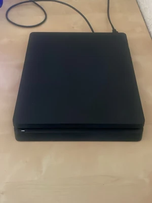 Sony PlayStation 4 Slim svart konsol - Säljer en svart PlayStation 4 Slim från Sony. Konsolen har en stilren, rektangulär design med rundade hörn och mattsvart finish. Perfekt för gaming och streaming, enkel att koppla in med HDMI och USB-portar på framsidan.