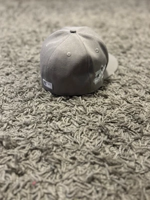 Grå LA Dodgers keps New Era - Säljer en stilren grå keps från New Era med LA Dodgers-logga broderad framtill. Klassisk rak skärm. Perfekt för dig som gillar sportig streetstyle och vill ha en clean look.