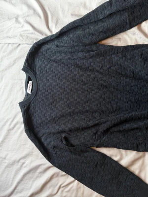 Mörkblå mönstrad tröja Weekd - Snygg mörkblå långärmad tröja från Weekday med diskret strukturmönster över hela plagget. Tröjan har rund halsringning och är tillverkad i ett mjukt material som känns skönt mot huden. Perfekt för dig som gillar stilrena basplagg med en twist.