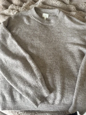Ljusbeige stickad tröja från H&M - Mysig ljusbeige stickad tröja från H&M med rund halsringning och ribbade muddar vid ärmslut och nederkant. Tröjan har en enkel och klassisk design som passar till det mesta. Perfekt för lager på lager under kyliga dagar.