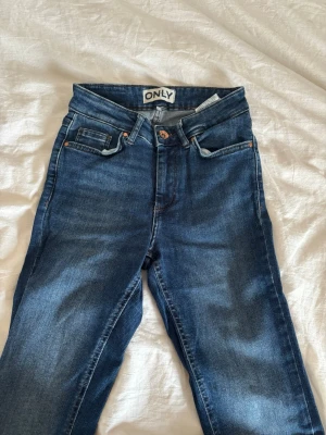 Blå Bootcut jeans från ONLY - Säljer ett par klassiska blå jeans från ONLY med bootcut  och femficksmodell. Jeansen har normal midja, knappgylf och snygga kontrastsömmar. Materialet är mjukt denim i bomull med lite stretch för extra komfort. Säljer då de inte kommer till använding💕