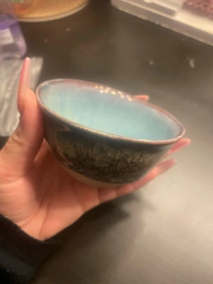 Liten keramikskål i blått och brunt - Unik liten keramikskål med rund form och glaserad insida i ljusblått. Utsidan har en blandning av bruna och beige toner med ett rustikt mönster. Perfekt för snacks, såser eller småprylar. Skålen har en handgjord känsla och mjuka kanter.