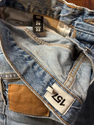 Ljusblå & Mörkblåa raka jeans från 157 och H&M - Säljer 2 par ljusblå och/eller mörkblåa jeans från 157 med klassisk rak passform och fem fickor. Jeansen har en snygg tvättad look, detaljer i kopparfärg och patch i brunt konstläder bak. Perfekta för en avslappnad och trendig stil.