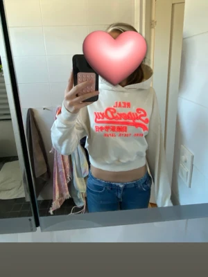 Vit cropped hoodie från Superdry - Säljer en vit cropped hoodie från Superdry med stor coral logga. Den är avklippt och omsydd sjävl men inget som märks på utsidan💕