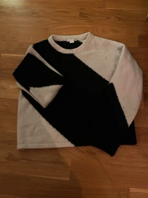 Stickad tröja med svartvitt mönster - Säljer en stickad tröja i vitt och svart med ett stort diagonalt blockmönster. Tröjan har rund halsringning och långa ärmar. Perfekt för dig som gillar grafiska kontraster och en avslappnad stil.