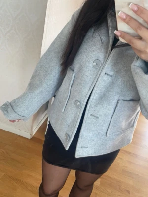 Ljusgrå ulljacka med stora fickor - Stilren ljusgrå jacka i ullmix med stora knappar och två rejäla fickor framtill. Jackan är från lager 157 i storlek XS, säljes då den ej kommer till användning. 