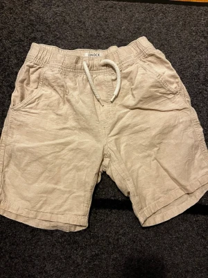 Beige linneshorts stl 140 Lindex - Säljer ett par beige linneshorts från Lindex med avslappnad passform. Shortsen har resårmidja med ställbar storlek på insidan. Snörning (bara för utseende), två sidofickor fram och två bakfickor. Stl 140