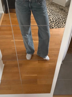 Ljusblå raka jeans med mellanhög midja - Säljer ett par ljusblå jeans med rak passform och hög midja. Jeansen har klassiska fem fickor och stängs med dragkedja och knapp. Perfekta till en avslappnad och trendig look. Materialet är denim 
