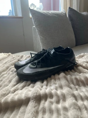 Nike svarta fotbollsskor med dobbar - Säljer ett par svarta Nike fotbollsskor med vit swoosh på sidan. Skorna har låg profil, snörning och slitstark ovandel i syntetmaterial. Dobbarna är utformade för bra grepp på gräsplan. Perfekta för dig som vill ha lätta och snabba skor på planen.