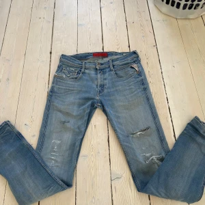 Replay Anbass ljusblå jeansbyxor - Säljer ett par Replay Anbass jeans i ljusblå tvätt med slitningar och detaljerade revor. Klassisk femficksmodell med dragkedja och knapp. Byxorna har normal passform och är i storlek W30 och L34. Pris kan diskuteras!