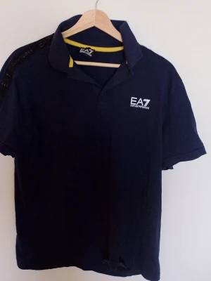Stilren EA7 Polo – Perfekt för både vardag och träning! - Snygg och bekväm EA7 Emporio Armani polo i mörkblått med subtila detaljer i svart och gult. Tillverkad i högkvalitativt material som andas och ger en skön känsla hela dagen. Passar utmärkt för både casual och sportiga tillfällen. Uppgradera din garderob med en tidlös klassiker från ett av världens mest välrenommerade märken! Kontakta mig för mer info eller köp direkt.   Den är storlek L men spassar perfekt för er som har M. Sågott som oandvänd