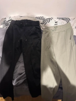 Två par mjukisbyxor, svart & grå - Säljer två par mjukisbyxor, ett par svarta och ett par ljusgrå. Båda har resår i midjan och dragsko för skön passform. Byxorna har raka ben och sidofickor. Perfekta för chill dagar eller när du vill vara bekväm.
