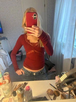 Röd långärmad topp med spets - Snygg röd långärmad topp med spetsdetaljer vid halsringningen och under bysten. Figurnära passform och v-ringad framtill.🤗