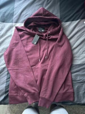 Vinröd hoodie från 157 - Snygg vinröd hoodie från 157 med klassisk känguruficka och justerbar dragsko i huvan. Tillverkad i mjukt material som känns skönt mot huden. Perfekt för dig som vill ha en enkel men stilren look.