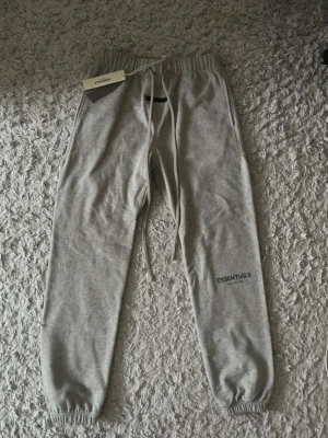 Grå Essentials mjukisbyxor - Snygga grå mjukisbyxor från Essentials med dragsko i midjan och resår vid bensluten. Byxorna har en relaxed fit och diskret logga på benet. Perfekta för chill dagar,Aldrig använt dem, helt nya med etiketter, fråga gärna om du har några frågor, priset kan diskuteras.