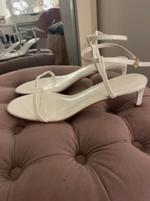 Vita sandaler med smala remmar - Stilrena vita sandaler från H&M med smala remmar och låg klack. Skorna har öppen tå och justerbart spänne runt om. Liten fläck på insidan (3 och 4 bilden). I storlek 38. Använda en gång