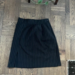 Svart pennkjol med ränder - Snygg svart pennkjol med tunna ränder och en liten slits framtill. Kjolen har hög midja och är ganska kort. Väldigt snygg men har tyvärr blivit för liten för mig