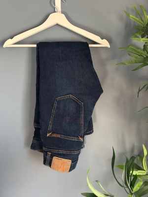 Mörkblå jeans från Nudie Jeans - Kvitto finns!     Snygga mörkblå jeans från Nudie Jeans med klassisk femficksmodell och kontrastsömmar. Jeansen har rak passform och är tillverkade i slitstark denim. Perfekta för dig som gillar en tidlös och clean look. 