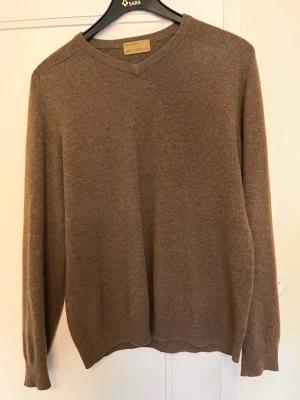 Brun cashmere tröja - Mjuk och stilren brun stickad tröja från The Collection. Tröjan har V-ringning, långa ärmar och ribbade muddar vid ärmslut och nederkant. Perfekt för lager på lager och enkel att matcha med olika outfits.