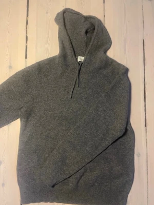Grå kashmir hoodie  - En enkel och stilren grå hoodie med huva och dragsko. Tillverkad i ett mjukt och bekvämt material (kashmir) som passar perfekt för en avslappnad look. Hoodien har långa ärmar och ribbade muddar vid ärmslut och nederkant. Sayless är märket