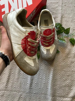 Japan gats 2006 - Tja! Säljer dessa gats sneakers i vitt och beige läder och mocka med en stor röd handmålad detalj på tån och matchande röda skosnören. Klassisk gummisula och låg silhuett. Perfekta för dig som gillar unika detaljer och streetwear-vibe.