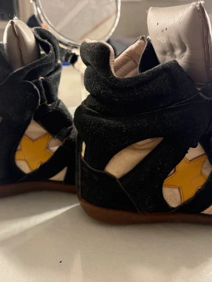 Svarta Isabel marant - Unika svarta Isabel marant skor perfekt till sommaren. Materialet är en mix av mocka och textil, med brun sula och vita partier. Perfekta för dig som vill sticka ut med din stil.