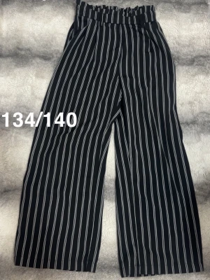 Svarta vida byxor med vita ränder - Snygga svarta byxor med vita vertikala ränder och hög midja med resår. Byxorna har en lös och rak passform som ger en trendig look. Perfekta för dig som gillar en avslappnad men ändå stilren stil.🌸Sparsamt använda. Storlek 134/140 