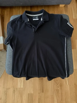 Mörkblå pikétröja från Pelle P - Klassisk mörkblå pikétröja från Pelle P med krage och korta ärmar. Tröjan har diskreta vita detaljer längs kragen och ärmslut samt logga på ärmen och nacken. Perfekt till en avslappnad och stilren look.