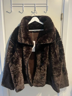 Pälsjacka Gina tricot - Säljer en fluffig mörkbrun teddyjacka med oversized passform och stor, bred krage. Jackan har knäppning framtill och är gjord i mjukt, fuskpälsliknande material.
