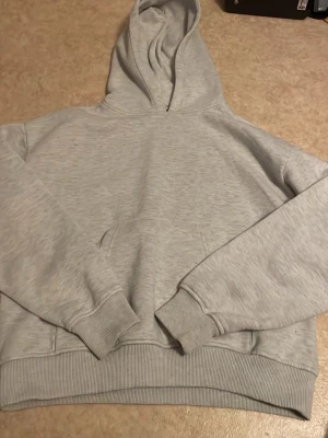 Ljusgrå basic hoodie - En stilren ljusgrå hoodie med huva och magficka. Tillverkad i mjukt sweatshirtmaterial med ribbade muddar vid ärmslut och nederkant. Perfekt för en avslappnad och enkel look.