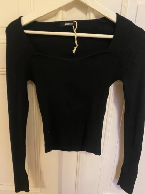 Svart långärmad topp Gina Tricot - Snygg svart långärmad topp från Gina Tricot med bred, något fyrkantig ringning. Modellen är tight och croppad, perfekt att styla med höga jeans eller kjol. Materialet känns mjukt och stretchigt.