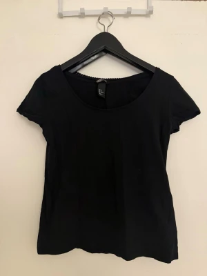 Svart kortärmad topp från H&M - En enkel svart topp från H&M med rund halsringning och korta ärmar. Tillverkad i mjuk bomull, perfekt att matcha med jeans eller kjol. Stilren och tidlös design som passar till många olika looks.