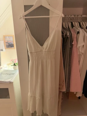 Vit sommarklänning med volang - Söt vit klänning med smala axelband och v-ringning. Klänningen har en smockad midja och volangdetaljer nertill, vilket ger en luftig och romantisk känsla. Perfekt för varma dagar och midsommarfirande. Även om det är storlek XL passar den mig som har S. Den är väldigt stretchig. 