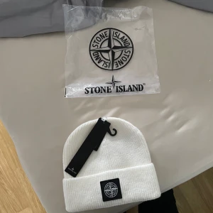 Vit ribbad mössa från Stone Island - Snygg vit ribbad mössa från Stone Island med deras ikoniska logga framtill. Perfekt för att hålla värmen under kyliga dagar. Stilren och enkel design som passar till det mesta.