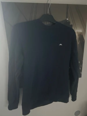 Mörkblå sweatshirt från J.Lindeberg - Snygg mörkblå sweatshirt från J.Lindeberg med rund halsringning och diskret logga på bröstet. Tröjan har långa ärmar och är tillverkad i mjukt bomullsmaterial för en bekväm känsla. Perfekt för en stilren och avslappnad look.