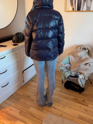 Mörkblå pufferjacka med huva - ❗️JACKAN ÄR XL BARNSTORLEK(170CM)❗️Säljer en mörkblå pufferjacka med glansig finish och huva. Jackan har en klassisk quiltad design med breda kanaler och dragkedja framtill. Perfekt för kalla vinterdagar och riktigt mysig att bära. Som man ser på sista bilden har jackan pyttelite slitage, men det är bara på tyger alltså går det inte in typ dunet! Så det påverkar varken värme eller funktion. Det syns knappast när jackan är på !!