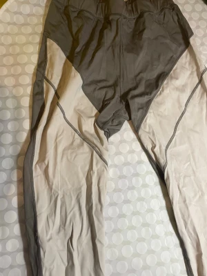 Grå och beige sportiga leggings - Säljer ett par snygga leggings i grått och beige med kontrastsömmar. De har en sportig look och är tillverkade i ett stretchigt material som sitter tajt mot kroppen. Perfekta för träning eller chill. Midjan är elastisk för extra komfort. Lappen är urtväddad så strl syns ej men om jag minns rätt är det strl M