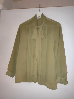 Vintage blus med knytband knytblus - Vintage stilren blus i ett tunt, lätt material med knytband i halsen och dekorativa veck framtill. Finns ingen storlek men bedömer den till S-M. Inköpt hos en vintagebutik.