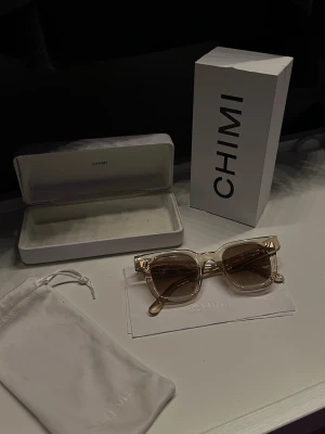 CHIMI 04 Ecru - Snygga solglasögon från CHIMI med transparent beige båge och ljusa glas. Rektangulär form som ger en modern vibe. Kommer med originalfodral och tygpåse. Perfekta för soliga dagar och en stilren look.