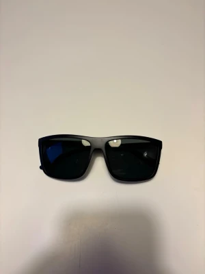 Rayban boyfriend liknande - Snygga svarta rayban boyfriend liknande solglasögon med rektangulära bågar och mörka glas. Klassisk och stilren design som passar till de flesta outfits.