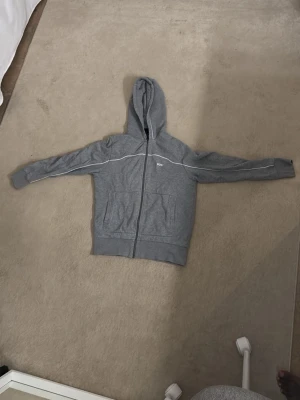 Grå zip hoodie med vita detaljer - Snygg grå hoodie från Bolt med dragkedja framtill och vita detaljer längs axlarna. Två stora fickor på magen och klassisk huva. Perfekt för en chill och avslappnad stil. Tillverkad i mjukt material som känns skönt mot huden. Storlek S men passar perfekt för XS